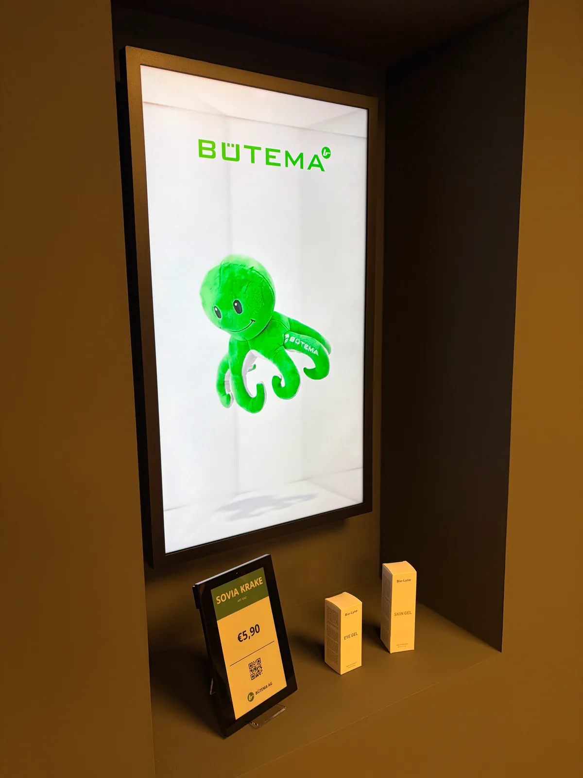 Hochformat-Display mit dreidimensional wirkender grüner Krake, darunter ein digitales Preisschild mit QR-Code